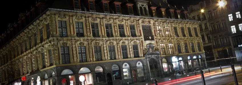 Façade ancienne éclairée et traînées lumineuses de circulation la nuit.