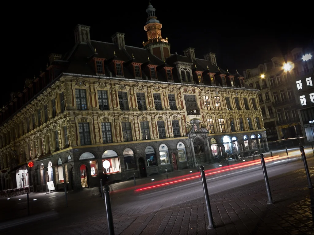 Façade ancienne éclairée et traînées lumineuses de circulation la nuit.