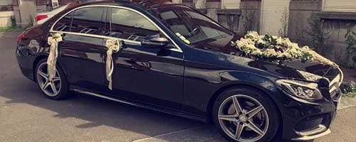 Berline Mercedes noire décorée de fleurs et de rubans pour un mariage.