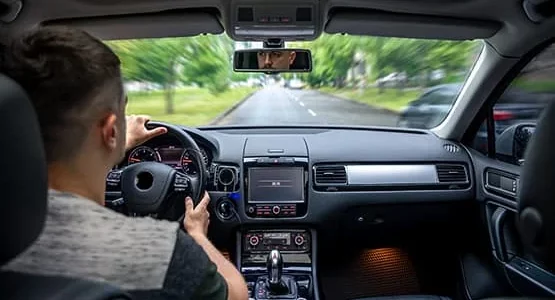 Conducteur au volant d’une voiture sur une route bordée d’arbres.