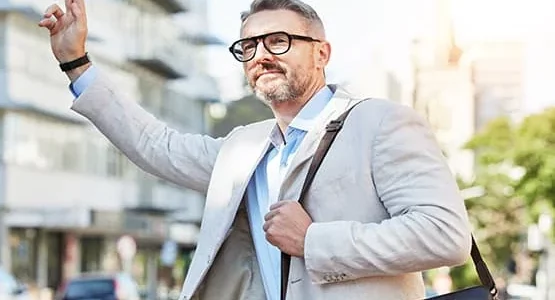 Homme en veste et lunettes levant la main dans la rue.