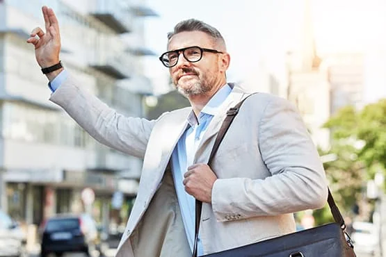Homme en veste et lunettes levant la main dans la rue.