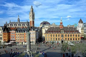 Place pavée entourée de façades anciennes avec une colonne centrale et un beffroi.