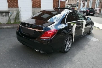 Berline Mercedes noire décorée de fleurs et de rubans blancs pour un mariage.