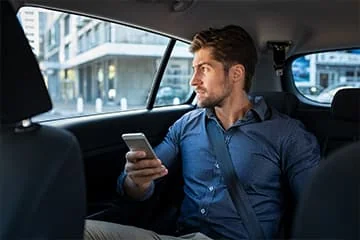 Transport chauffeur VTC Lille Passager tenant un téléphone et regardant par la fenêtre à l’arrière d’une voiture.