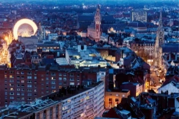 Panorama de toits, de tours et d’une grande roue éclairés à la tombée de la nuit.