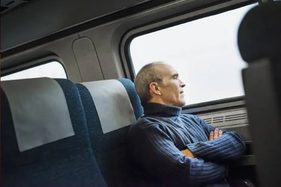 Voyageur assis près de la fenêtre d’un train, les bras croisés.