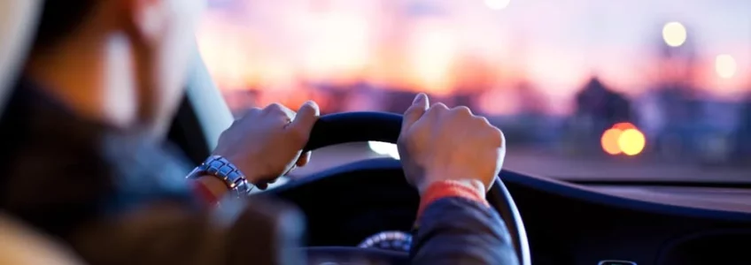 Conducteur tenant le volant d’une voiture au coucher du soleil.