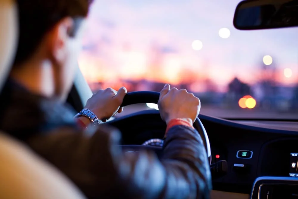 Conducteur tenant le volant d’une voiture au coucher du soleil.